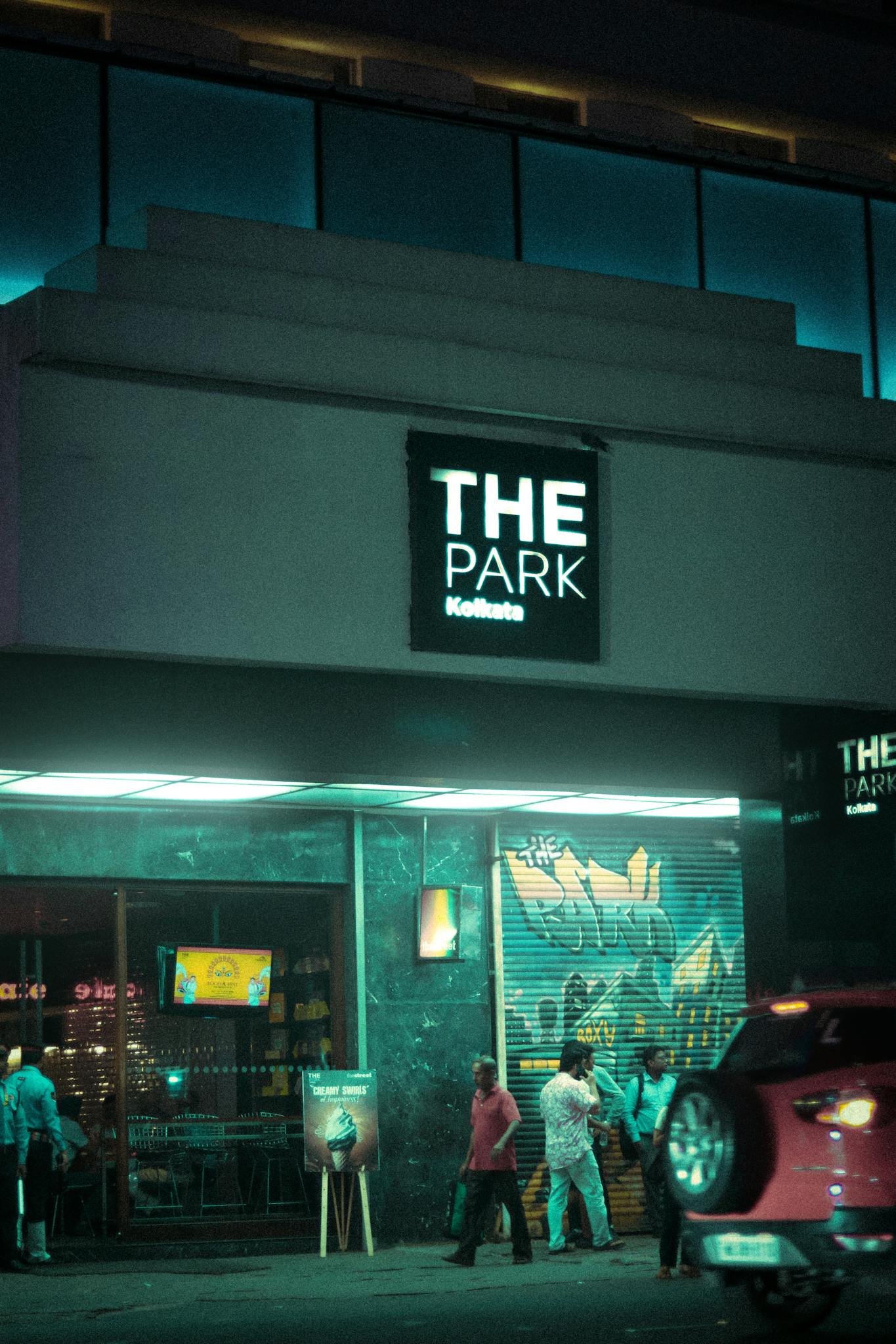 Illuminated entrance of The Park hotel in Kolkata with pedestrians nearby at night.